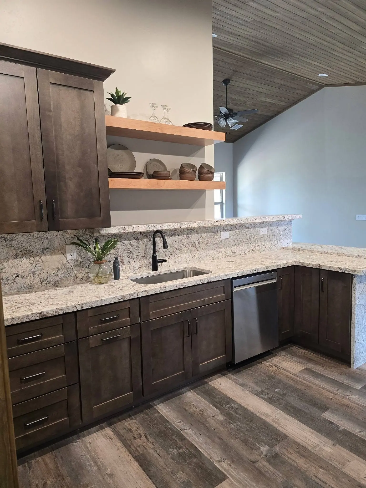 Stained shaker kitchen cabinets with floating shelves and granite counters