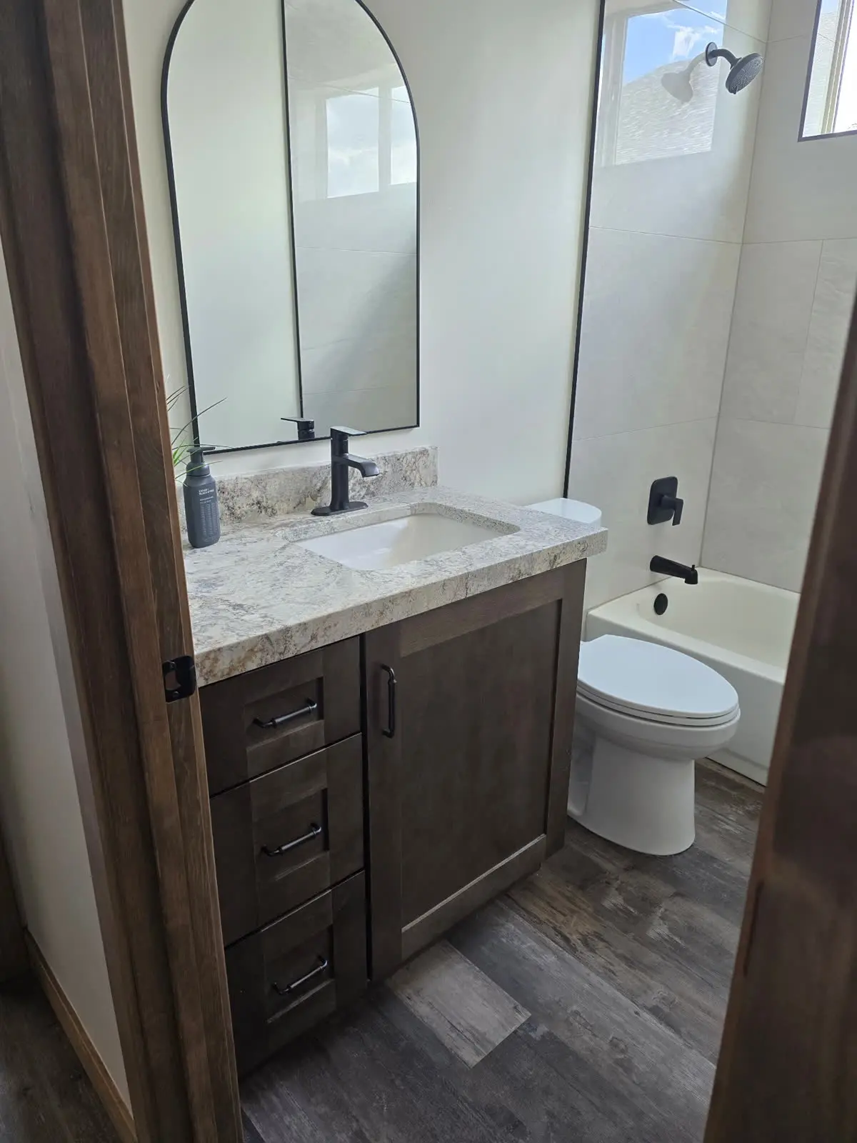 Dark wood bathroom vanity with arched mirror and tub by DC Cabinets