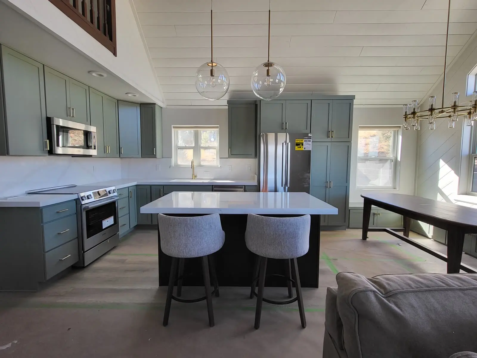 Green kitchen cabinets with island and pendant lights by DC Cabinets