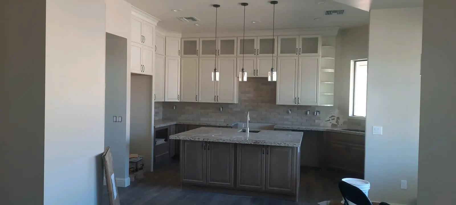 White kitchen cabinets with gray island and pendant lights by DC Cabinets