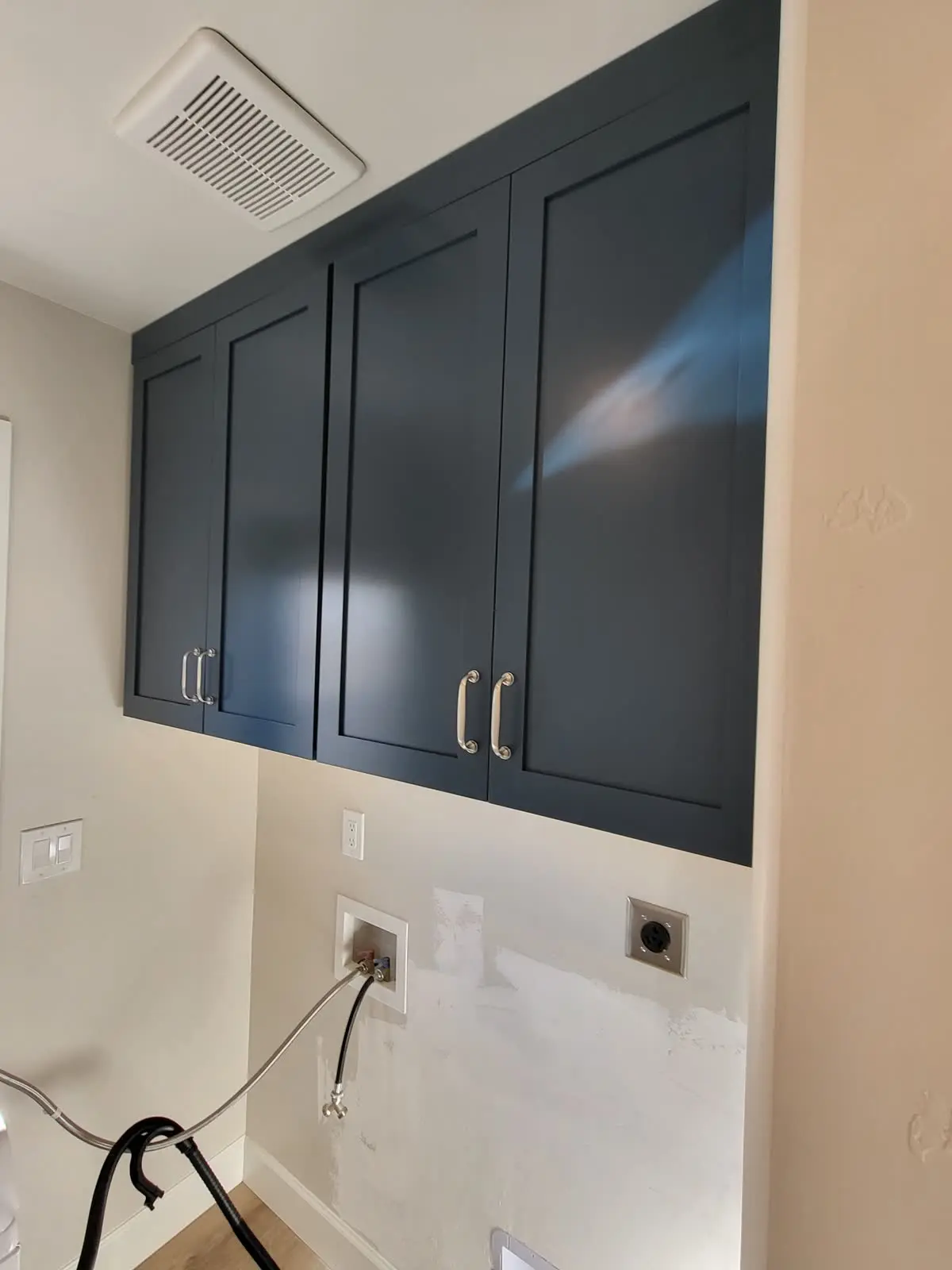 Navy blue laundry room wall cabinets above washer hookups by DC Cabinets