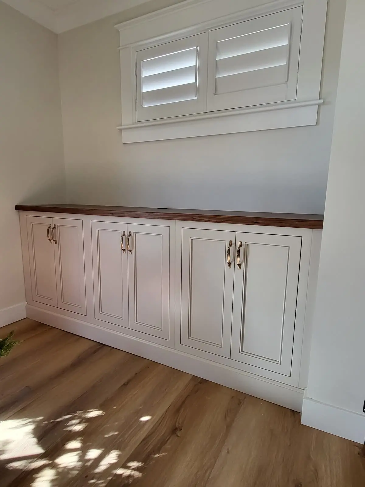 White built-in cabinet with wood top under window by DC Cabinets